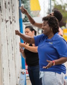 Mary Ferris (right), of the Rotary Club of Detroit, scrapes paint from the facade of Irma Fuentes' hardware store in Detroit.